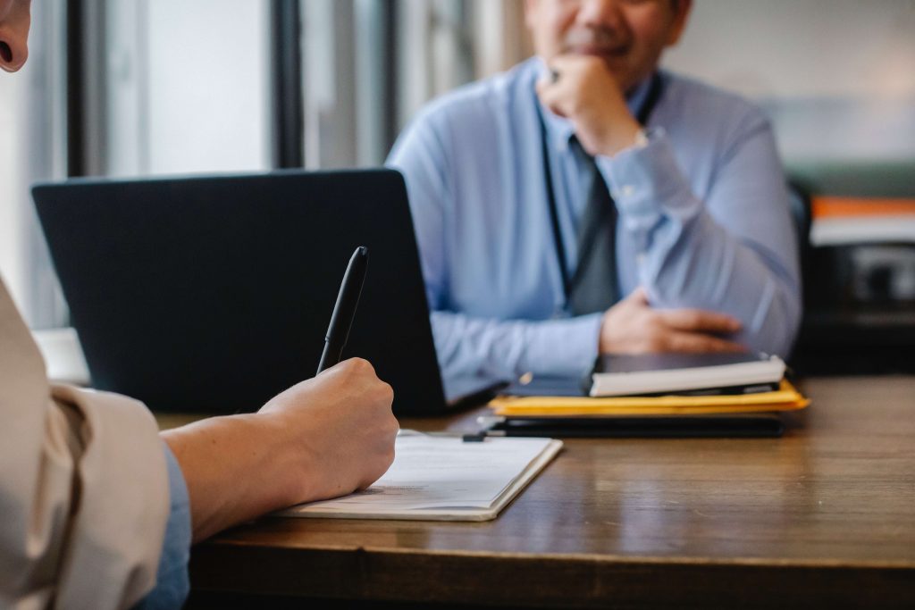 Hiring talent: A person sat at a desk writing on a clipboard opposite an interviewer.